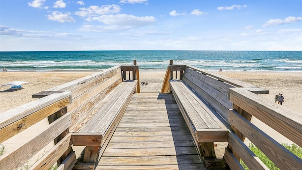 Ein hölzerner Steg führt zu einem Strand mit freiem Blick auf das Meer.