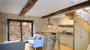 Une cuisine moderne avec un mur en pierre, des poutres en bois, un coin bar et un escalier.