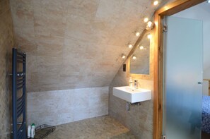 A modern bathroom with a sloped ceiling, a built-in sink, and a shower area. - Dove House Cottage 1 (Witney)