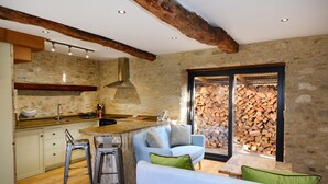 A rustic kitchen with stone walls, wooden beams, and a built-in stove. - Dove House Cottage 1 (Witney)