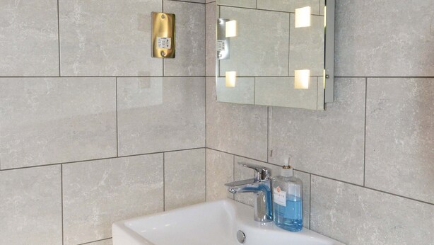 A bathroom with a white sink, a mirror with lights, and a toilet. - Dove House Cottage 1 (Witney)