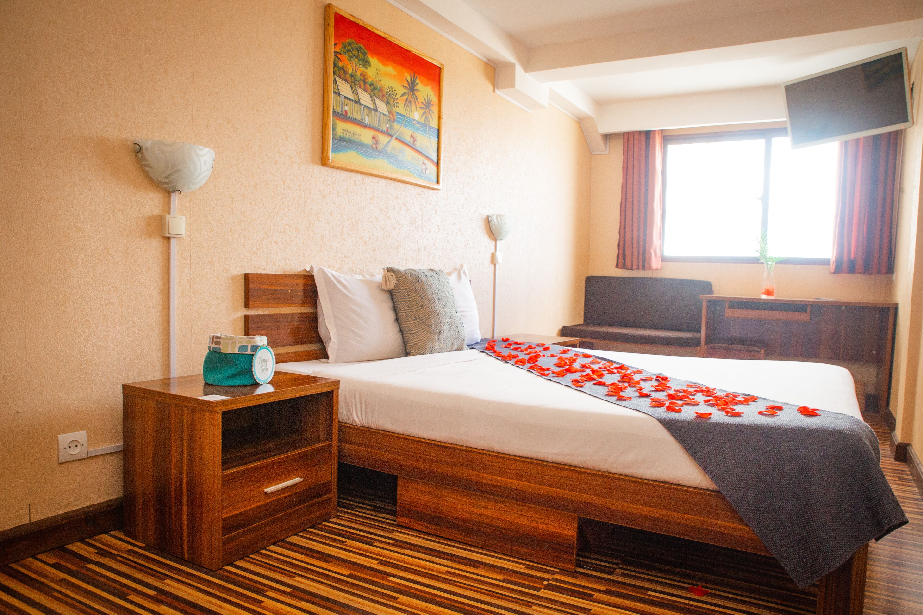 Une chambre d’hôtel avec un lit en bois, une table de chevet, un bureau, une télévision et un tableau au mur.