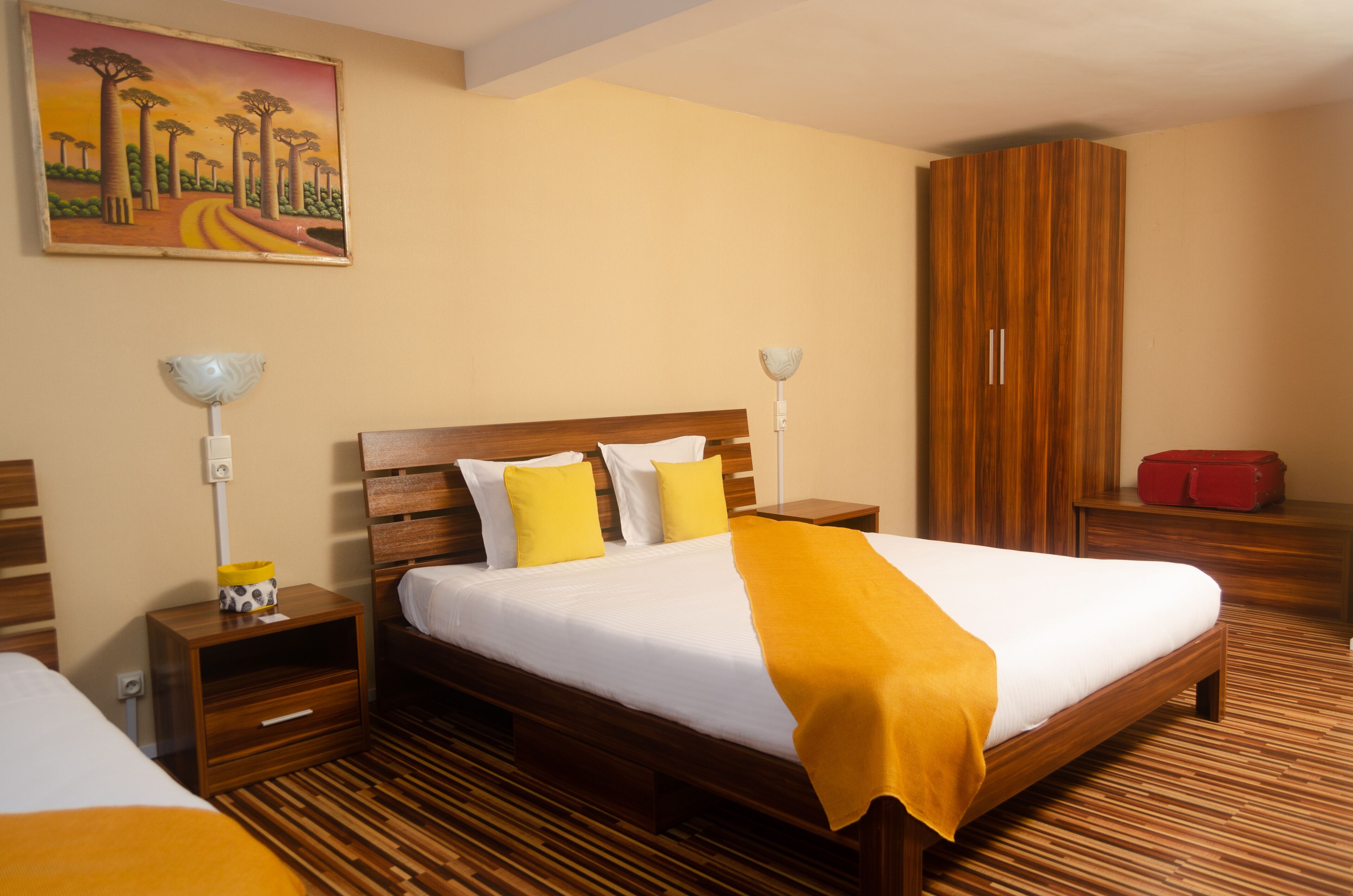 A hotel room with a wooden bed, two bedside tables, a nightstand, a wardrobe, and a painting on the wall.