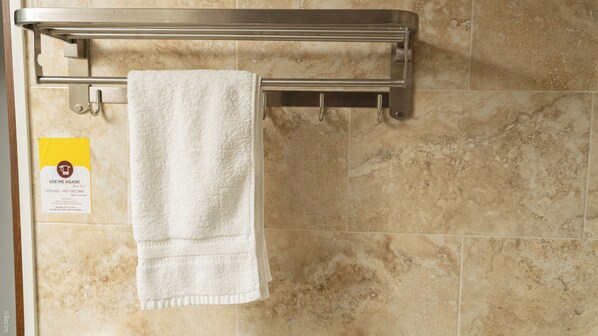 Un baño con un perchero que sostiene una toalla blanca, un cartel con indicaciones y paredes de azulejos.