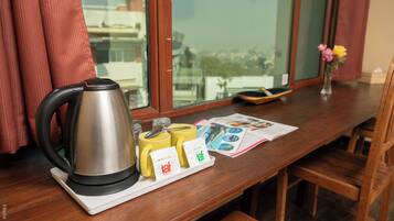 A wooden table with a kettle, yellow mugs, a spoon, a magazine, and a small vase with flowers.