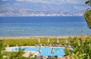 Une piscine avec des chaises longues et des parasols, une plage et une vue lointaine sur la ville.