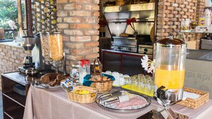 Ein Frühstücksbuffet mit verschiedenen Speisen und Getränken, eine Ziegelwand und Küchengeräte im Hintergrund.