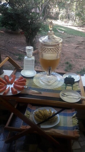 An outdoor dining setup with a large glass punch bowl, a glass carafe, and a plate of sliced fruit.