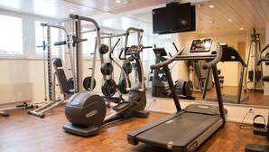 Ein Fitnessraum mit Cardio-Geräten, Krafttrainingsmaschinen und einem an der Wand befestigten Fernseher.