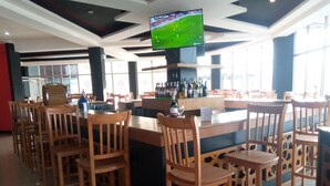 A bar area with wooden chairs and tables, a television mounted on the ceiling, and a bar counter with bottles. - Bruhway Hotel (Addis Ababa)