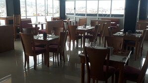 A dining area with tables and chairs, large windows, and a view of the city. - Bruhway Hotel (Addis Ababa)
