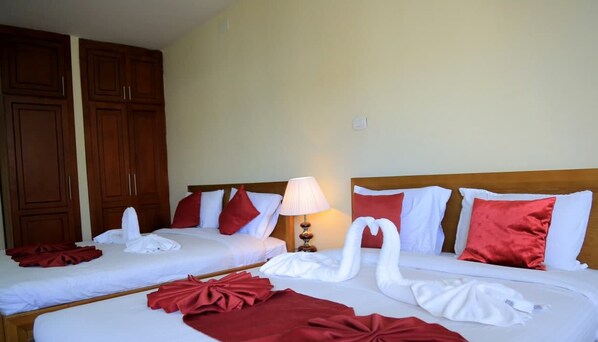 A hotel room with two beds, each with white linens and red pillows. There is a lamp between the beds, and a wooden wardrobe is visible to the left. - Bruhway Hotel (Addis Ababa)