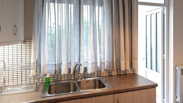 A kitchen with a double sink, a window with sheer curtains, and a view of the outside. - Classy & Spacious Flat near Marina of Patra (Patras)