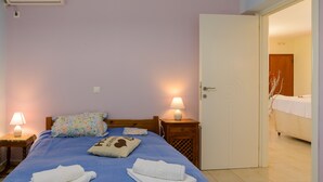 Una cama bien hecha con ropa de cama azul, dos lámparas de noche y una puerta que da a otra habitación.