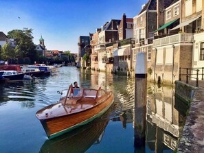 A narrow canal with a wooden boat, buildings on the right, and a church steeple in the background. - Arthouse B&B Dordrecht (Dordrecht)
