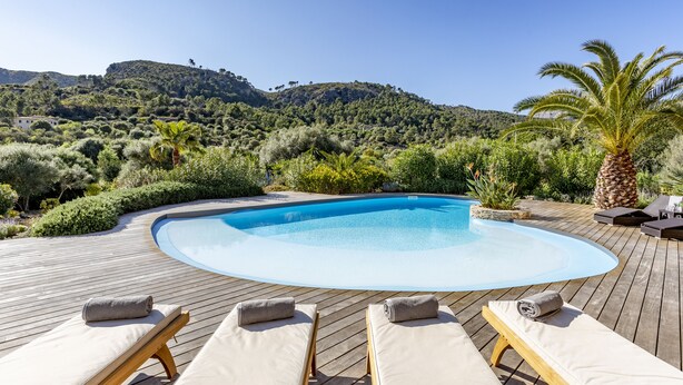 A wooden deck with a swimming pool, lounge chairs, and a view of a hilly landscape. - Luxurious finca with large pool in a unique location (Andratx)
