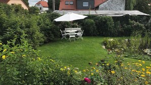 Ein Garten mit Rasen, einem Tisch mit Stühlen und einem überdachten Bereich.