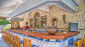 A bar area with a stone wall, wooden bar counter, and wicker chairs.