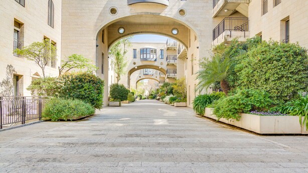 Un patio con un arco central, rodeado de abundante vegetación y un sendero pavimentado.