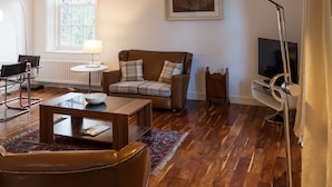 A living room with a sofa, armchair, coffee table, lamp, and a television. - Apartment 3 The Grove (Durham)