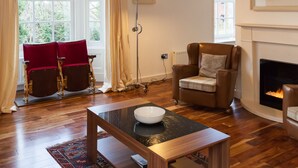 A living room with a fireplace, a wooden coffee table, a red armchair, and a floor lamp. - Apartment 3 The Grove (Durham)