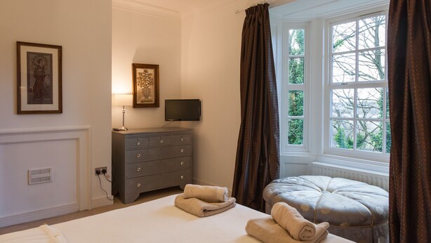 A bedroom with a bed, a dresser, a television, and a window with curtains. - Apartment 3 The Grove (Durham)