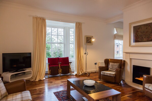 A living room with a television, a fireplace, and a large window with curtains.