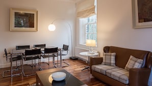 A living room with a brown leather sofa, a dining table with four chairs, a lamp, and a framed picture on the wall. - Apartment 3 The Grove (Durham)