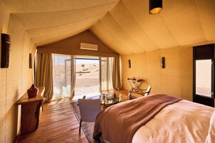 Una habitación con cama, escritorio, silla y vista a un paisaje desértico por la ventana.