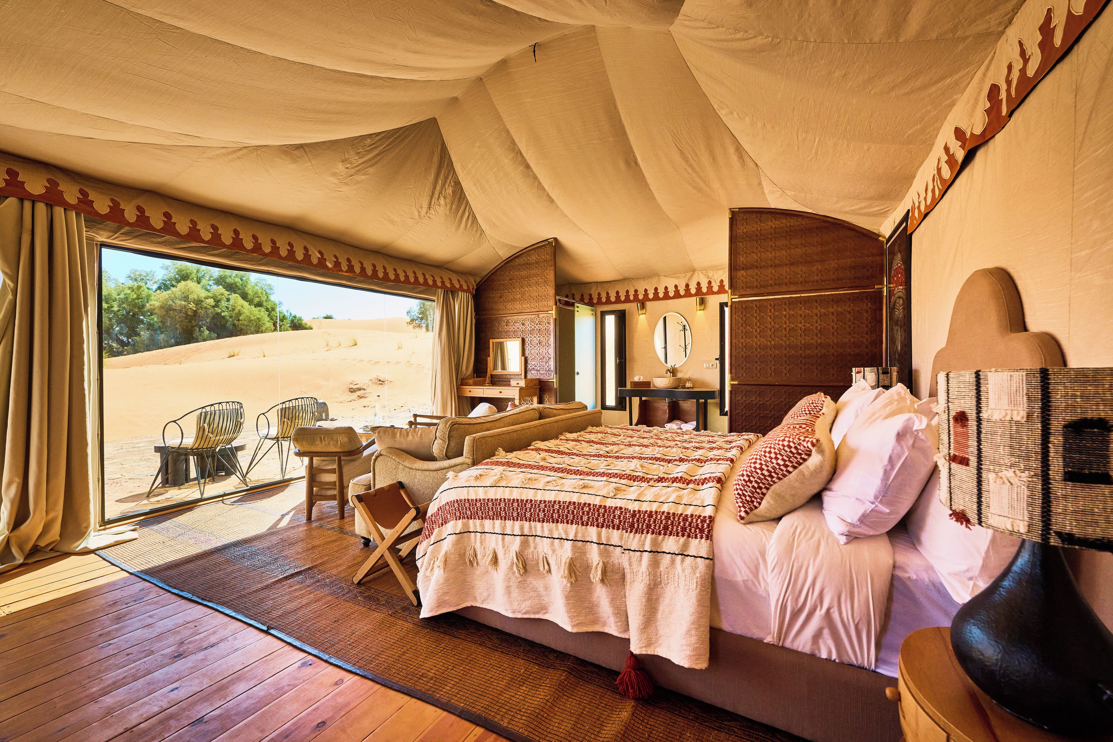 Una habitación amplia con una cama grande, piso de madera, vista del desierto a través de una ventana y un rincón de descanso con sillones.
