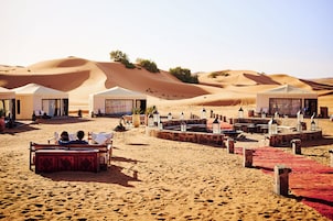 Un campamento en el desierto con tiendas de campaña, mobiliario exterior y un paisaje arenoso.