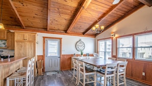 A wooden interior with a dining table and chairs, a kitchen area with wooden cabinets, and a clock on the wall. - 5377- Memorial Blvd. - Family-Friendly KDH Retreat Near the Beach (Kill Devil Hills)