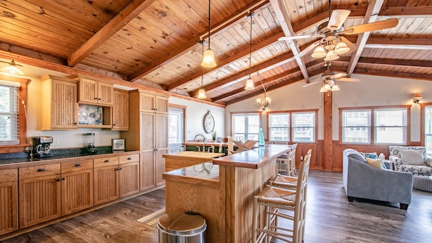 A spacious kitchen with wooden cabinets, a central island, and a bar area. There is a dining area with a sofa and chairs. - 5377- Memorial Blvd. - Family-Friendly KDH Retreat Near the Beach (Kill Devil Hills)