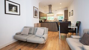 A modern living room with a sofa, a dining table with chairs, and a kitchen area in the background. - Apartment 4 The Grove (Durham)