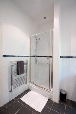 A modern bathroom with a glass-enclosed shower, a towel rack, and a small trash bin. - Apartment 4 The Grove (Durham)