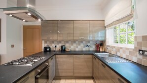 A modern kitchen with a gas stove, stainless steel range hood, wooden cabinets, a black countertop, and a window with a view of greenery. - Apartment 4 The Grove (Durham)