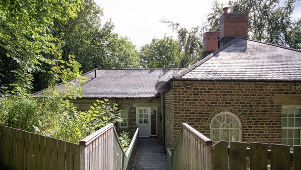 A brick house with a wooden staircase leading to a door, surrounded by trees. - Apartment 4 The Grove (Durham)