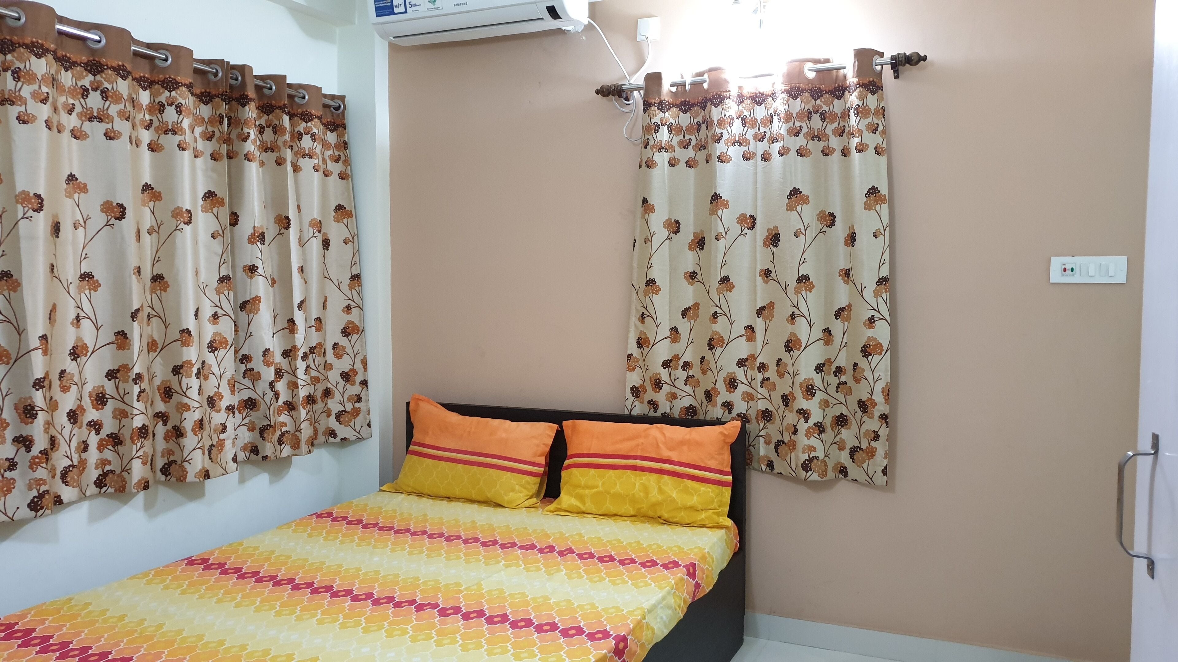 A bedroom with a bed, floral curtains, and a wall-mounted air conditioner.
