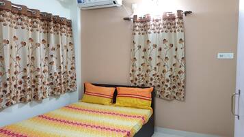 A bedroom with a bed, floral curtains, and a wall-mounted air conditioner.