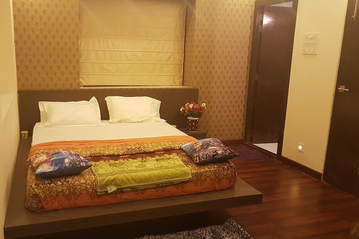 Una cama con una colcha estampada, dos almohadas y un florero con flores sobre una mesita de noche.