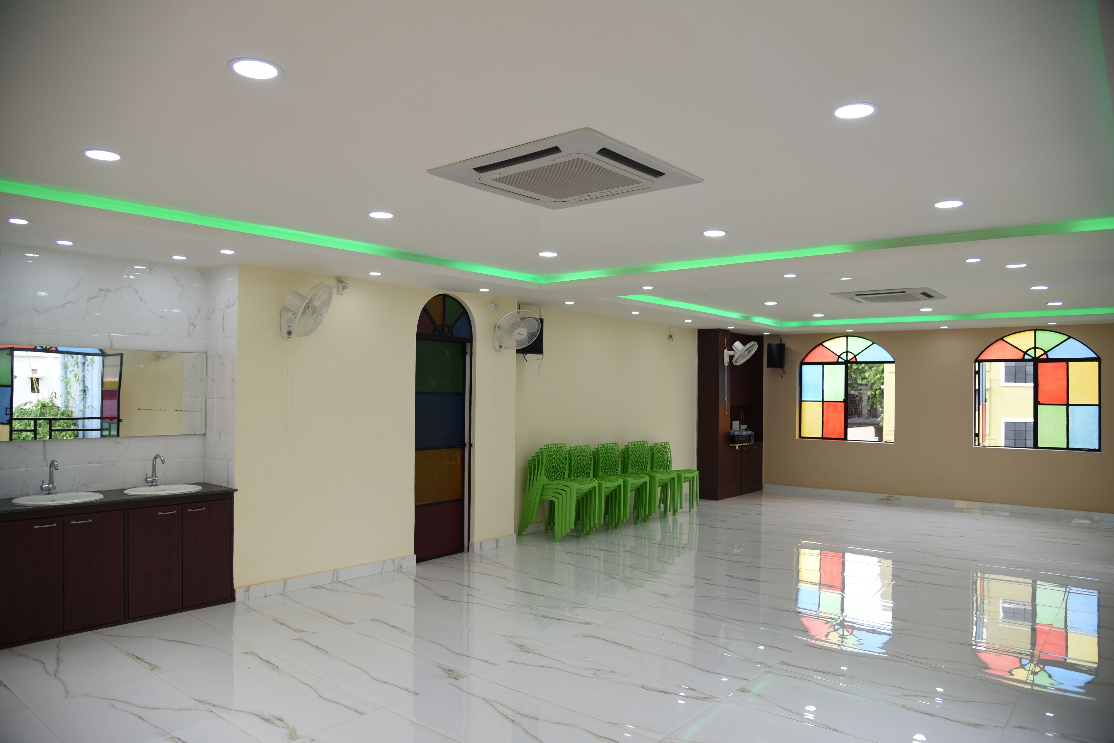 A spacious room with a marble floor, a large mirror, a sink, and green plastic chairs.