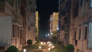 A nighttime view of a residential building with a central pathway lined with lights and pebbles, flanked by buildings with balconies and windows.