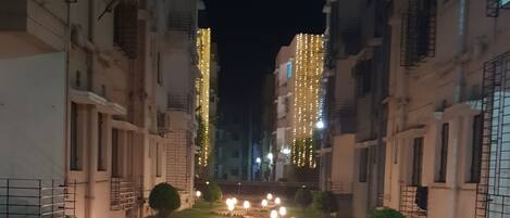 A nighttime view of a residential building with a central pathway lined with lights and pebbles, flanked by buildings with balconies and windows.