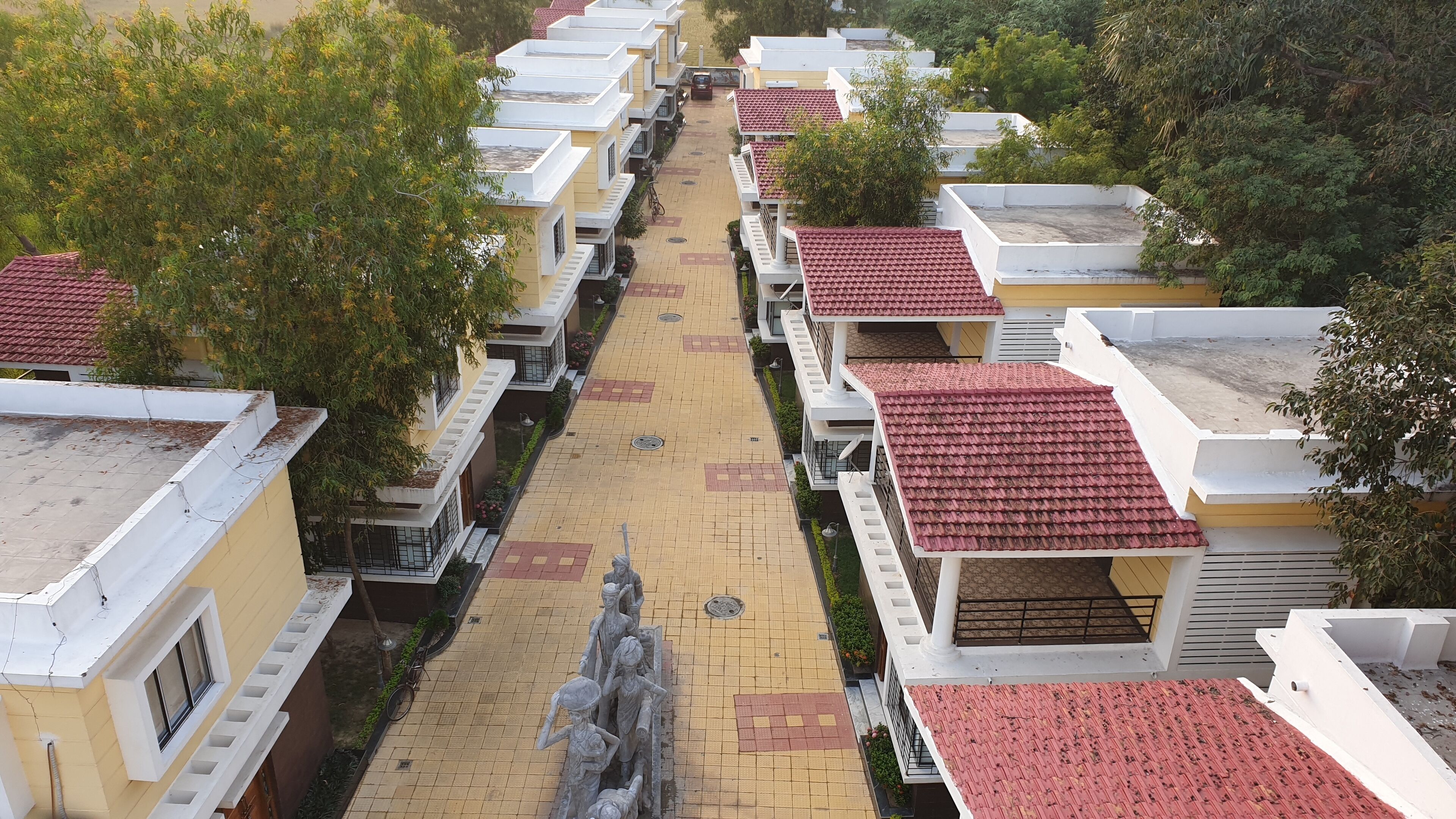 A row of residential buildings with red-tiled roofs, a central pathway, and a statue in the middle.