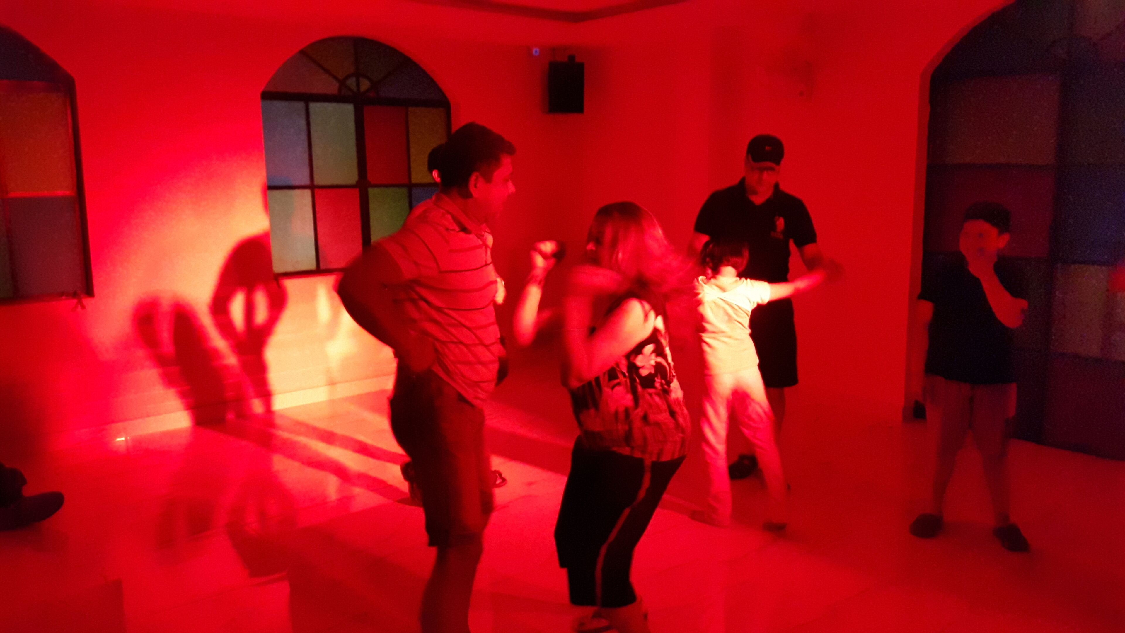 A dance class in a room with arched windows and red lighting.