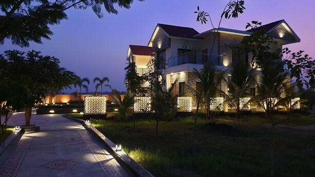A modern multi-story building with a well-lit facade, surrounded by palm trees and a landscaped garden.