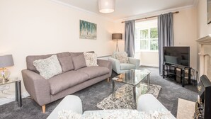 En moderne stue med en grå sofa, en lyseblå lænestol, et sofabord i glas og et fladskærms-tv.