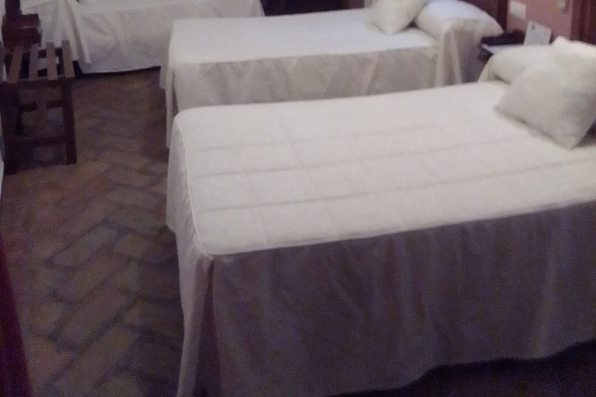 A room with two single beds, a wooden chair, a desk, and a wall-mounted TV.