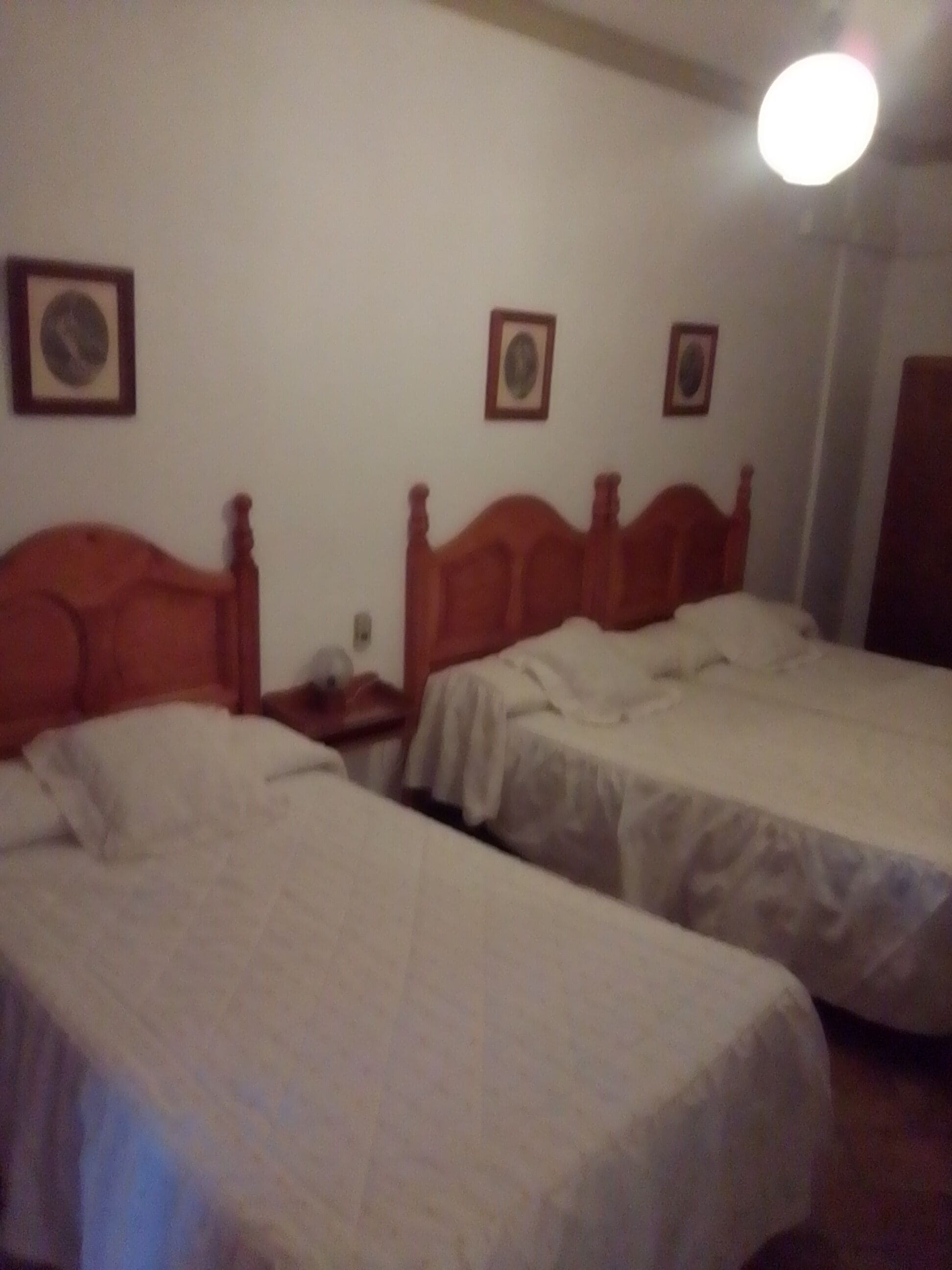 A room with two single beds, wooden headboards, white bedding, and framed pictures on the wall.