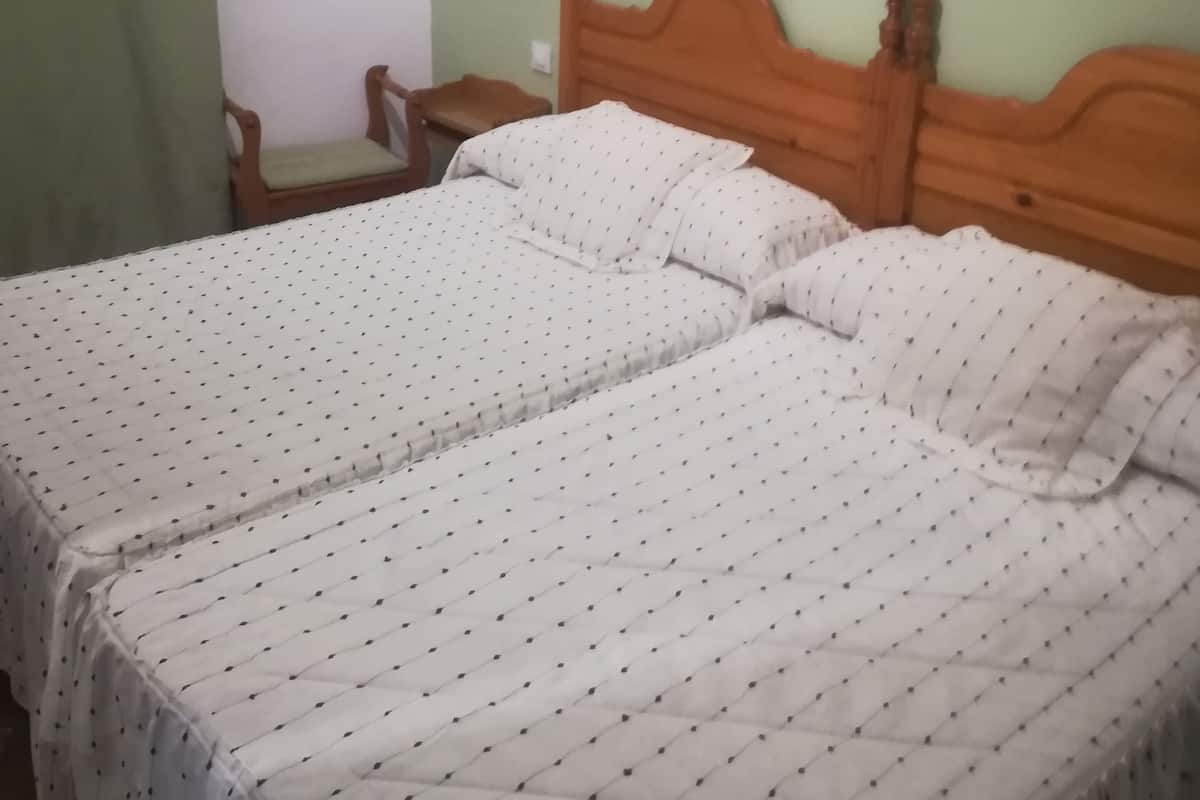 A double bed with a quilted white bedspread and two pillows, a wooden headboard, a small bedside table, and a wall-mounted mirror.